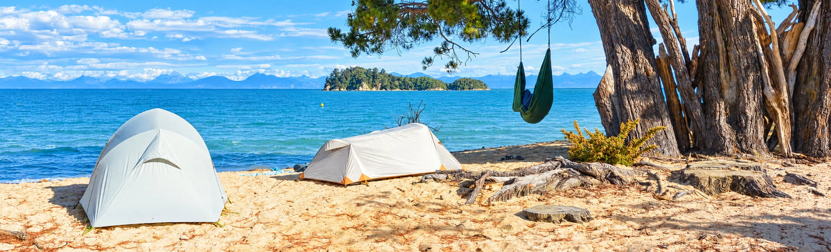Two tents and a hammock pitched on a beach beside clear water
