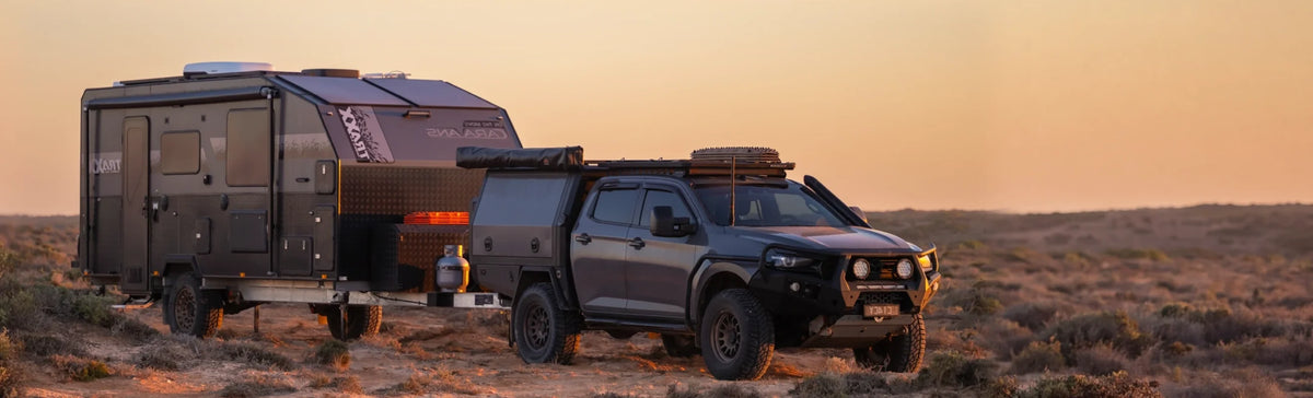 Off road caravan towed by a 4WD ute set up in outback scrub at dusk
