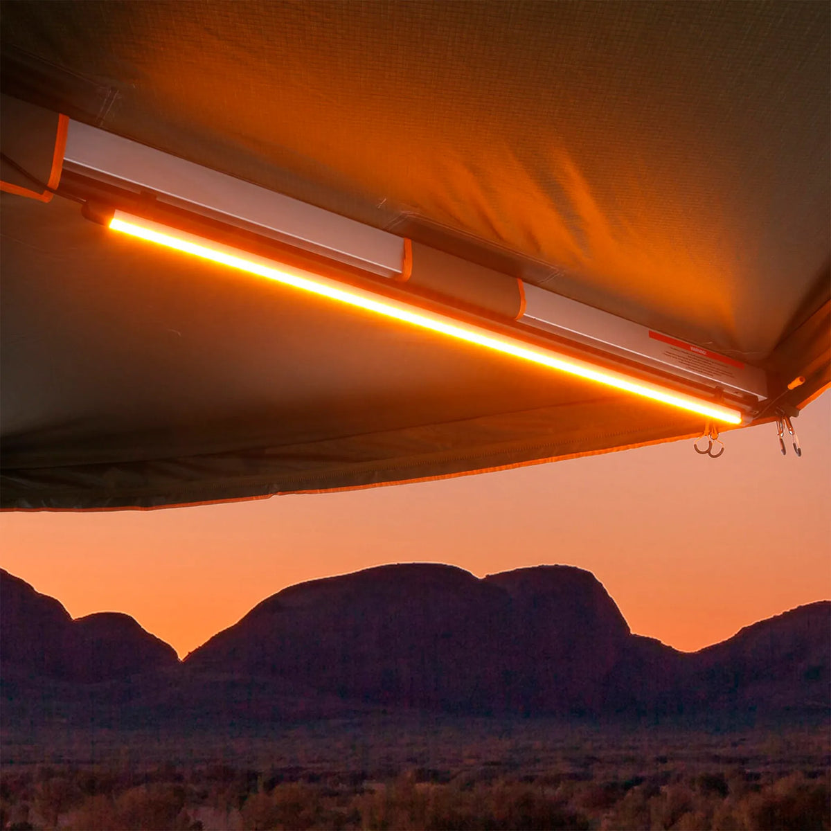 Hardkorr 100cm LED light bar mounted beneath an awning, glowing orange with mountains beyond at sunset.