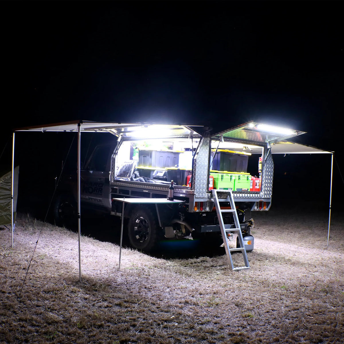 Hardkorr 100cm LED light bar kit casting white light over a camper trailer kitchen and the ground at night.