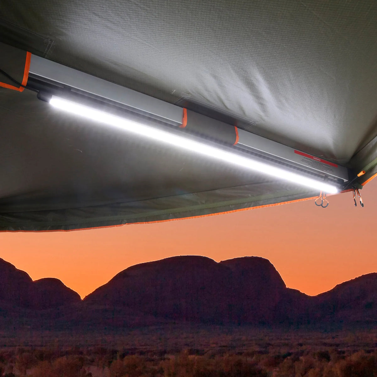 Hardkorr 100cm LED light bar mounted beneath an awning, glowing white with mountains beyond at sunset.