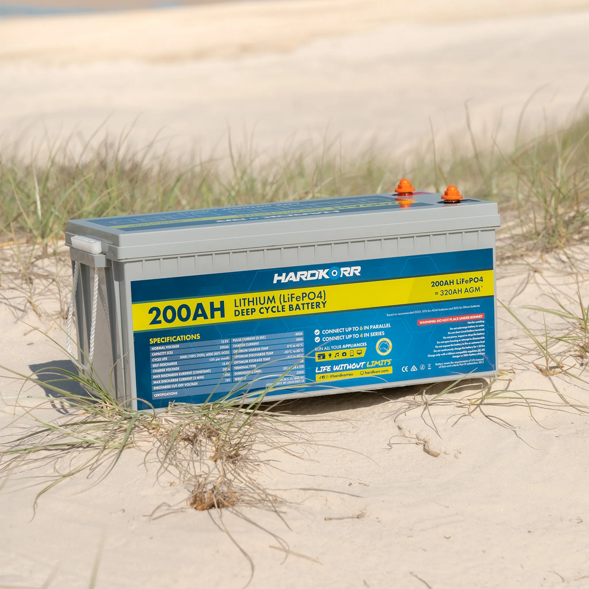 Hardkorr 200Ah 12V lithium battery on beach sand with its rear specifications label and terminal covers visible.
