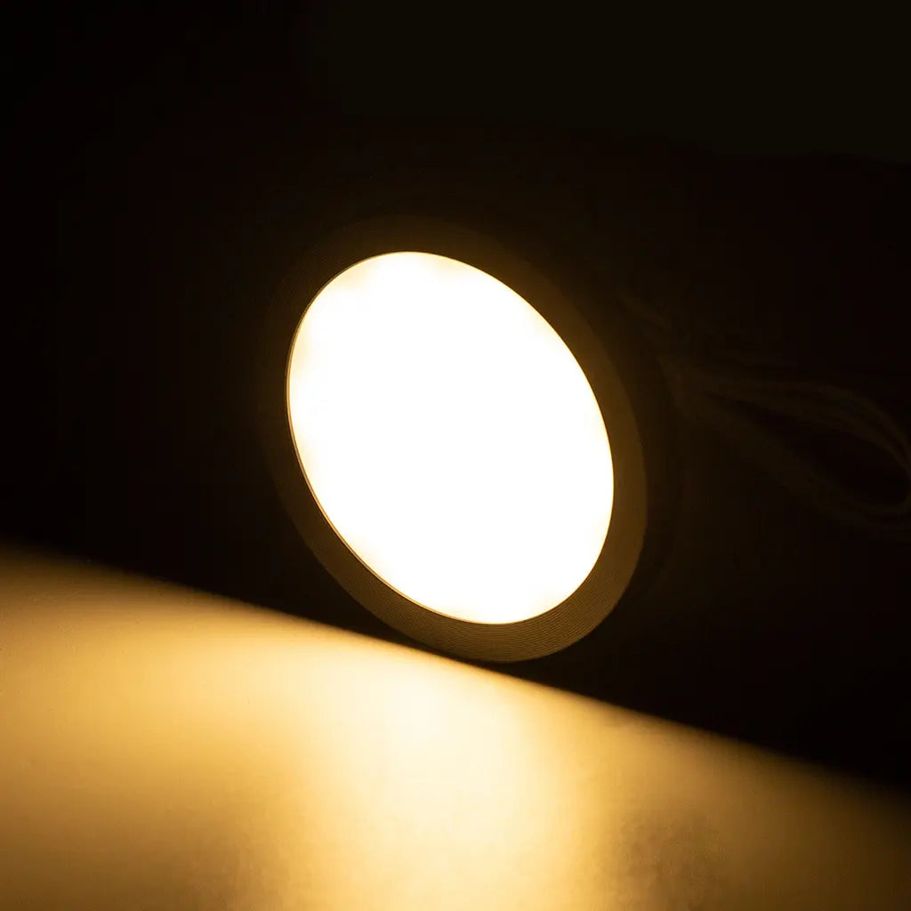 Rekcharge 12V black warm white LED downlight lit up with warm light falling on the surface below.