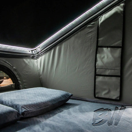 Bushwakka Shack rooftop tent interior close up with white strip lighting, a mattress, pillow and storage pockets.