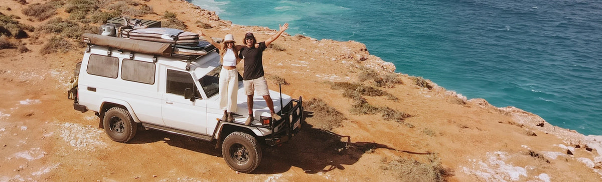 Two people on the roof rack of a white 4WD troop carrier parked on a coastal headland
