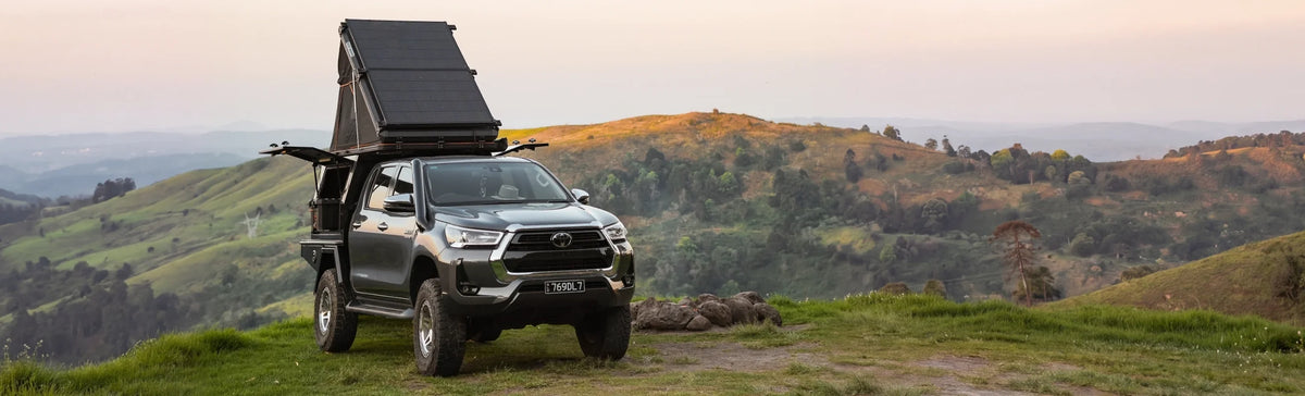 Hard shell rooftop tent opened on a 4WD ute parked on a green hilltop