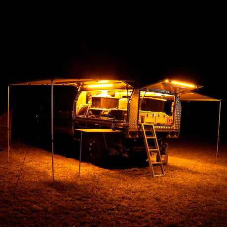 Hardkorr 100cm LED light bar kit casting orange light around a camper trailer and its awning at night.