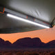 Hardkorr 100cm LED light bar mounted beneath an awning, glowing white with mountains beyond at sunset.