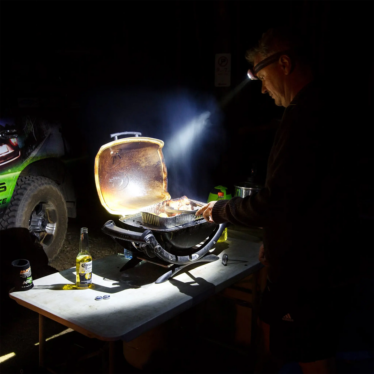 Hardkorr 145 lumen headtorch lighting a portable barbecue while a man cooks at night.