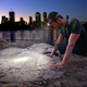 Hardkorr 145 lumen headtorch lighting a rock beside the water with city buildings in the background.