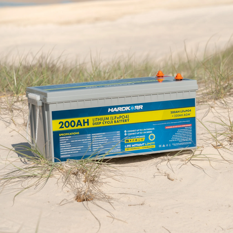 Hardkorr 200Ah 12V lithium battery on beach sand with its rear specifications label and terminal covers visible.