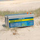 Hardkorr 200Ah 12V lithium battery on beach sand with its rear specifications label and terminal covers visible.