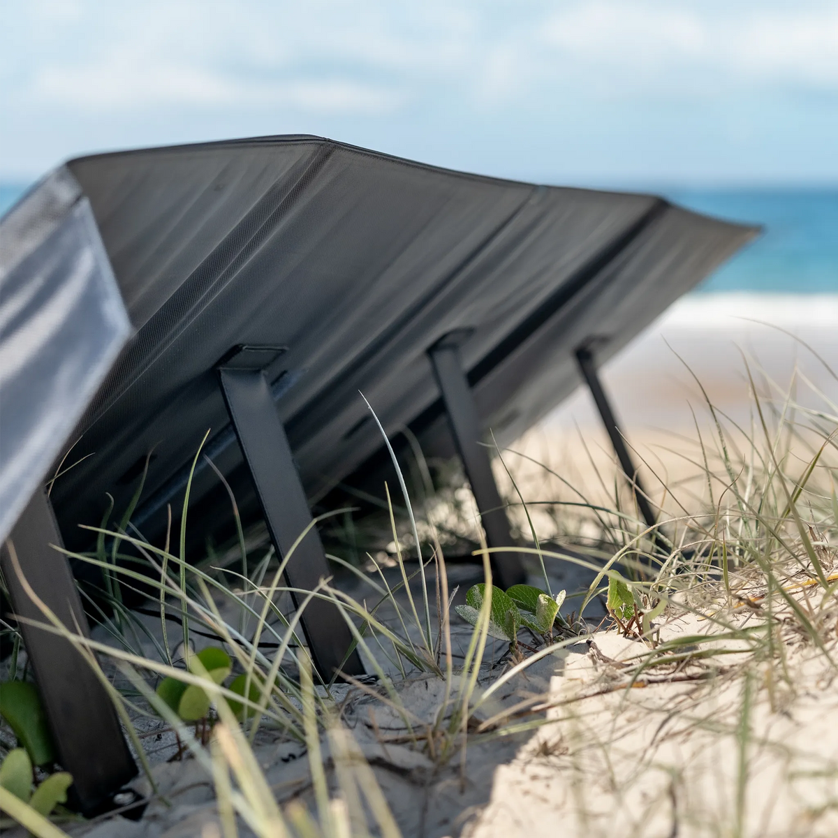 Hardkorr 200W 12V portable solar mat rear view with black backing and support legs resting in dune grass.