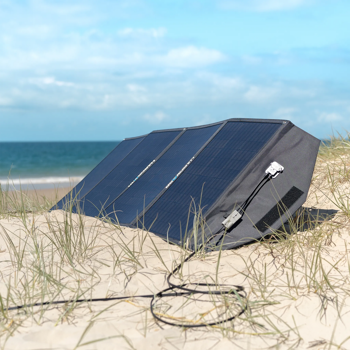 Hardkorr 200W 12V portable solar mat set up on sand dunes with its cable extended beside the beach.