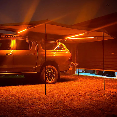 Hardkorr 3 strip LED awning light kit casting orange light beneath a vehicle awning at night.