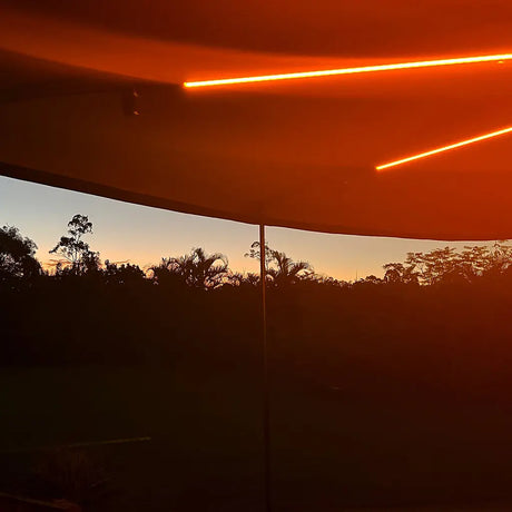Hardkorr 3 strip LED awning light kit glowing orange along the awning arms at dusk.
