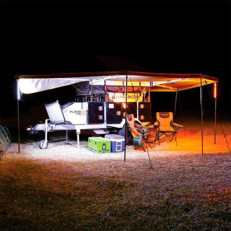 Hardkorr 4 bar LED camp light kit lighting a camper trailer awning in white and orange beside chairs.