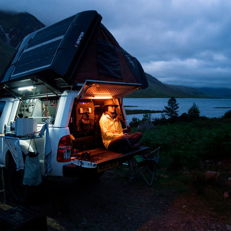 Hardkorr 50cm LED light bar kit lighting a vehicle's rear cargo area where a person sits beside a lake.