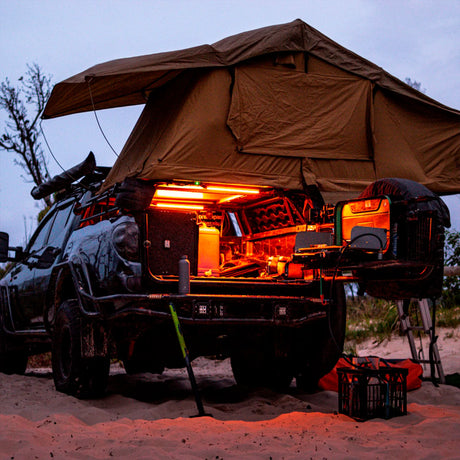 Hardkorr 50cm LED light bars casting orange light over an open ute tray beneath a rooftop tent.