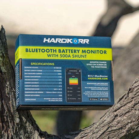 Hardkorr Bluetooth battery monitor box resting in a tree fork with rear specifications and a phone app illustration.