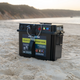 Black Hardkorr battery box on beach sand with a phone connected on the lid and the display lit.