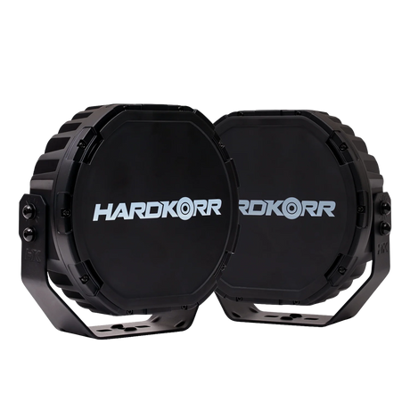 Pair of Hardkorr XD Series 9 inch LED driving lights with branded black covers fitted and mounting brackets below.
