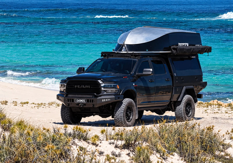Black RAM ute with a canopy and rooftop tent parked on a beach