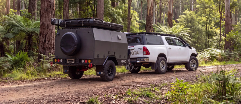 Off-road camper trailer hitched to a white Toyota HiLux on a forest track