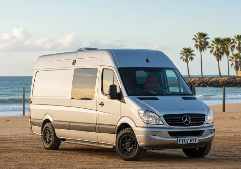 Silver Mercedes-Benz Sprinter campervan parked on a beach beside palm trees