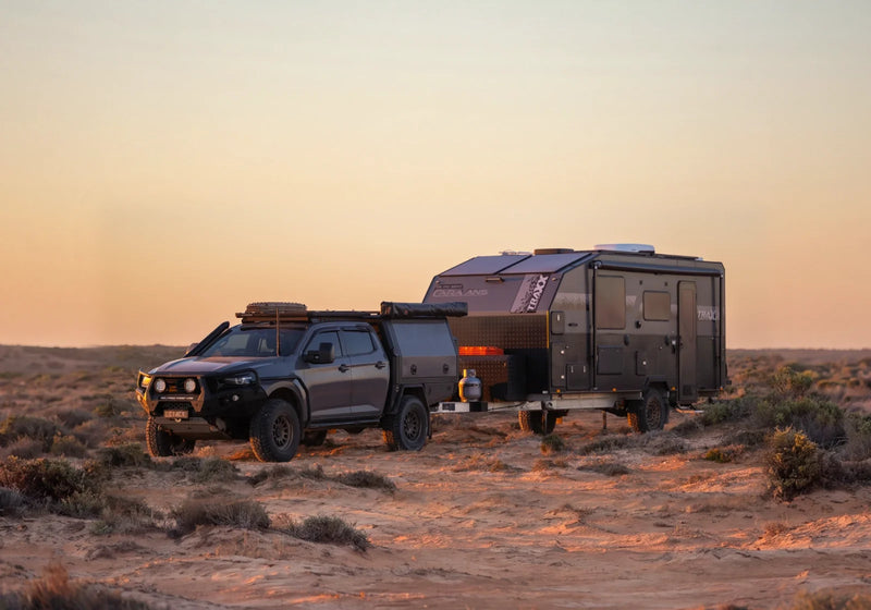 Dual-cab ute towing an off-road caravan across the outback at sunset