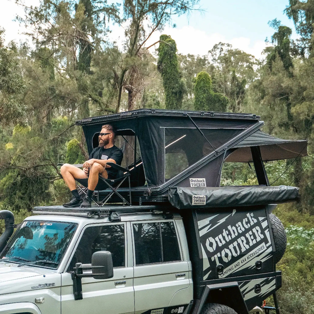 Outback Tourer 1550 Z Rooftop Tent open front right view with a person seated on a platform.