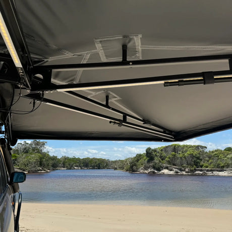 Outback Tourer Drivers Side 270 Awning underside view with support arms, LED lights above a beach river.