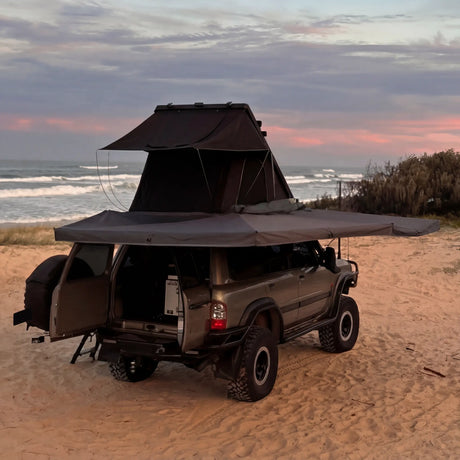 Outback Tourer Drivers Side 270 Plus Awning back corner view with a rooftop tent open beside the ocean.