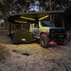 Outback Tourer Drivers Side 270 Plus X-Tend Awning open and lit on a vehicle at a beach campsite.
