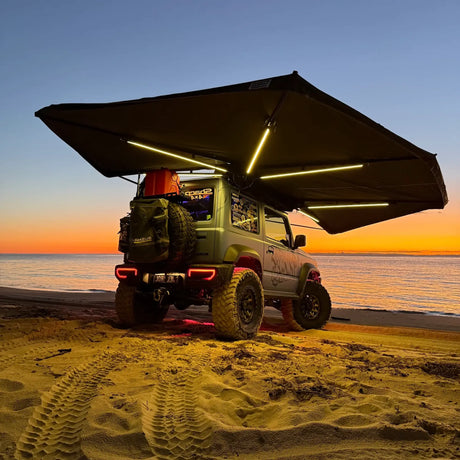 Outback Tourer Drivers Side 270 Plus X-Tend Awning open with led light bars beside the ocean.