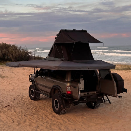Outback Tourer Passenger Side 270 Plus Awning back corner view with a rooftop tent open beside the ocean.