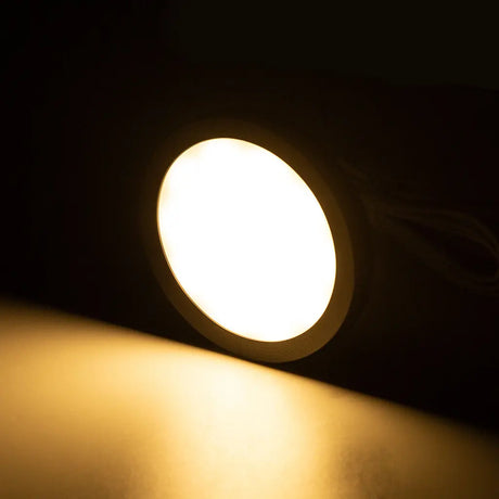 Rekcharge 12V black warm white LED downlight lit up with warm light falling on the surface below.