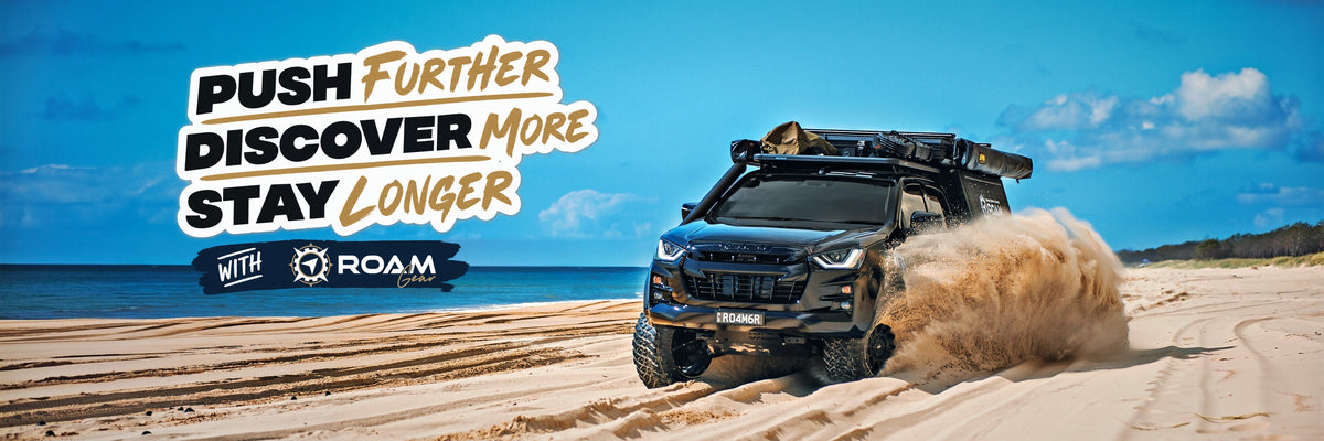 Black Isuzu D-Max on the beach with the Push Further, Discover More, Stay Longer slogan and the Roam Gear logo